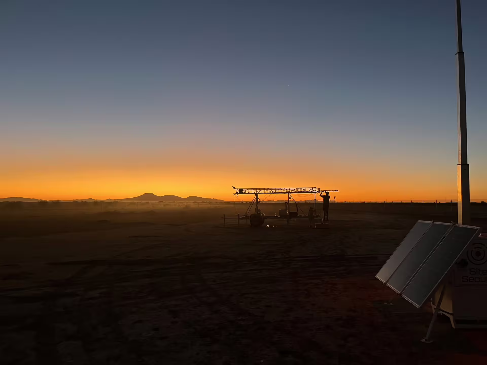 Researcher backlit by setting sun with wind rig