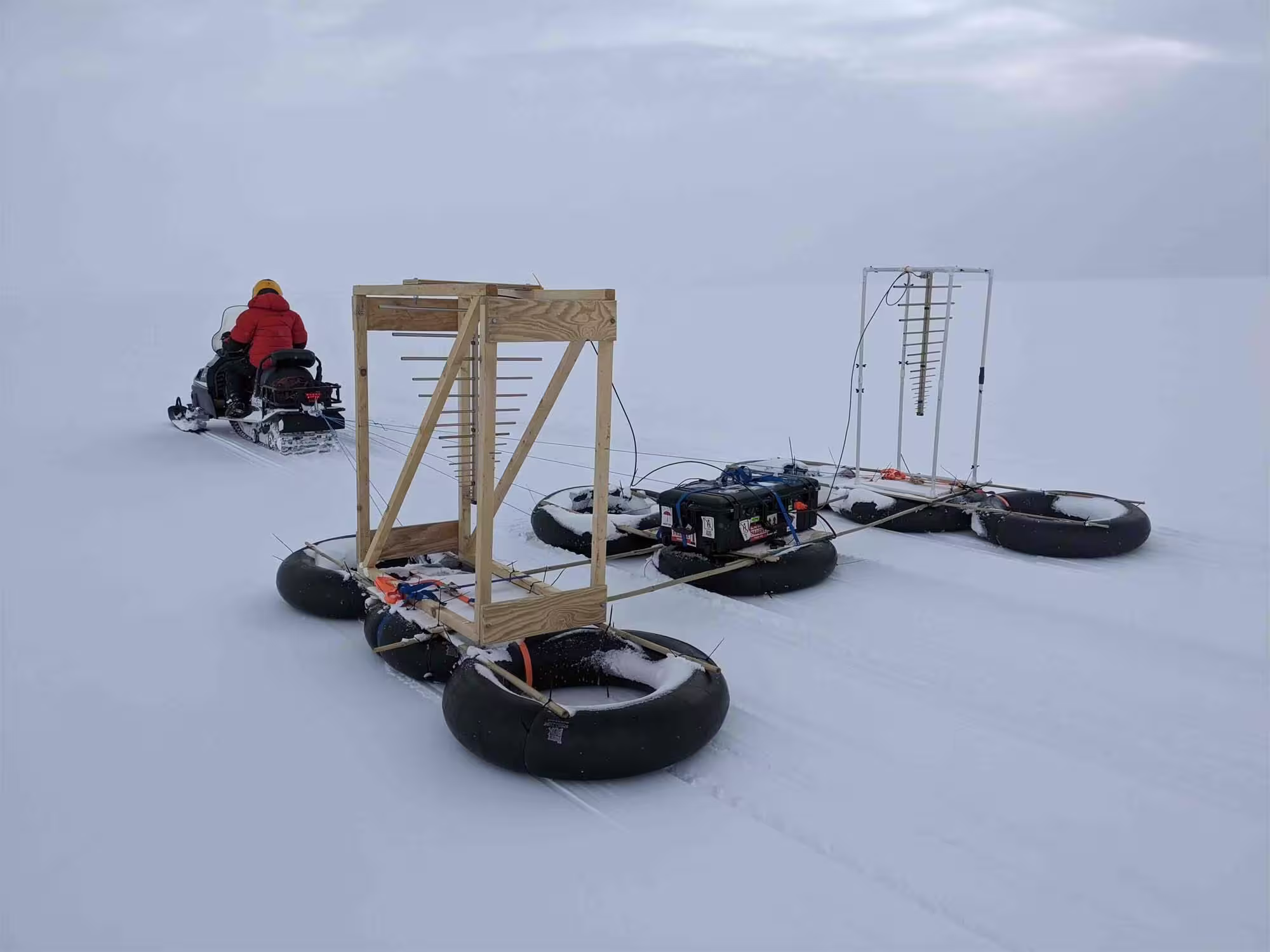 A researcher on a snowmobile pulling a large radar instrument behind it