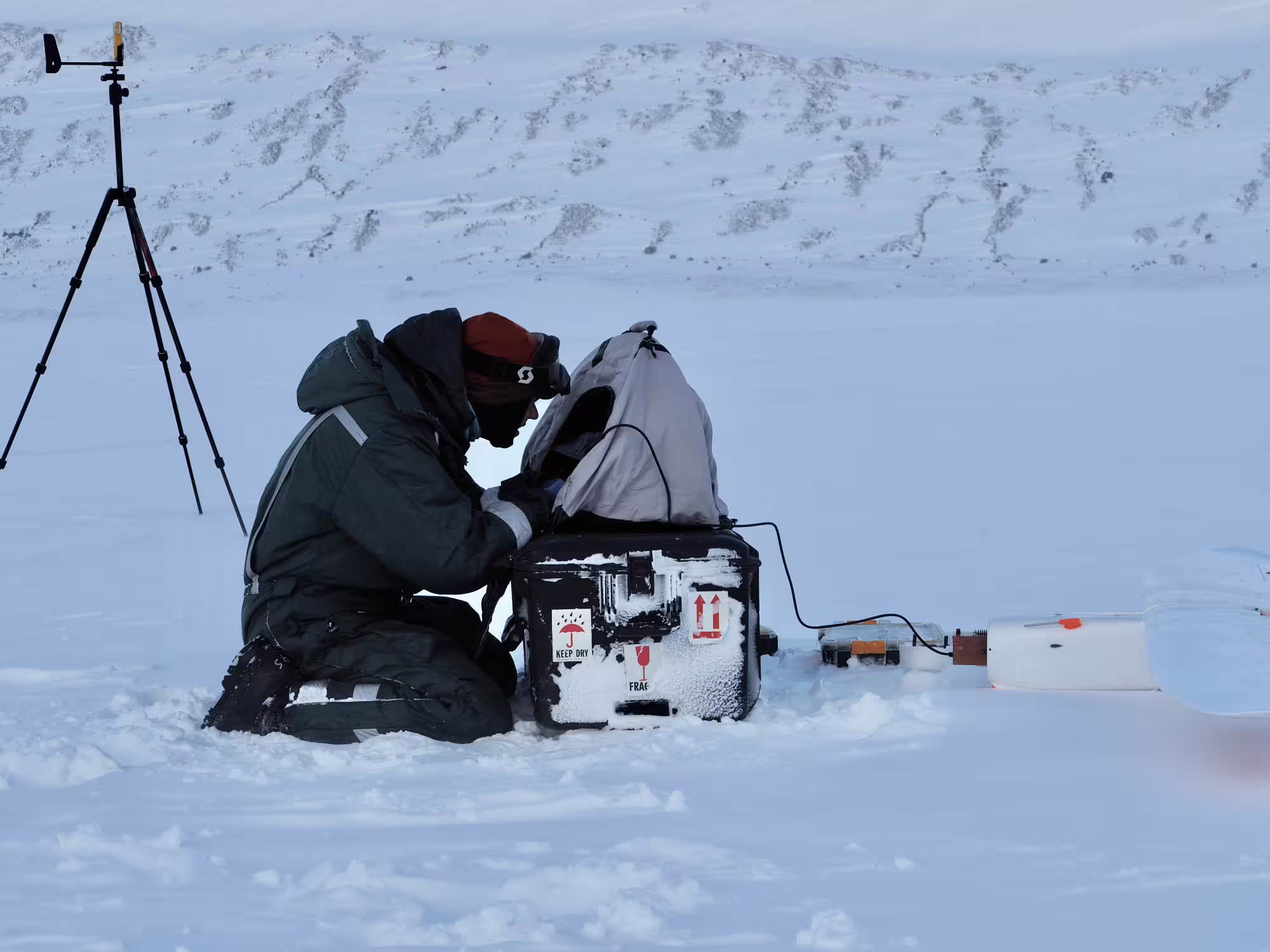 A researcher looking on a computer attached to a radar instrument in the snow